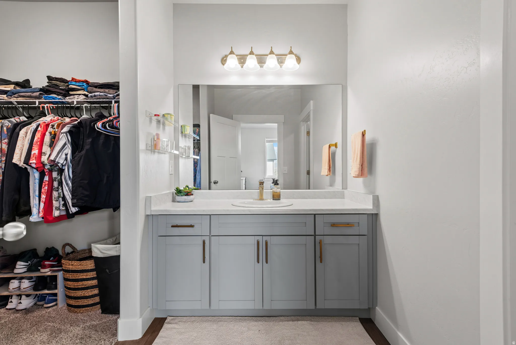 Bathroom vanity featuring a single sink, light gray cabinetry with gold-toned hardware, a white countertop, and an overhead four-light fixture