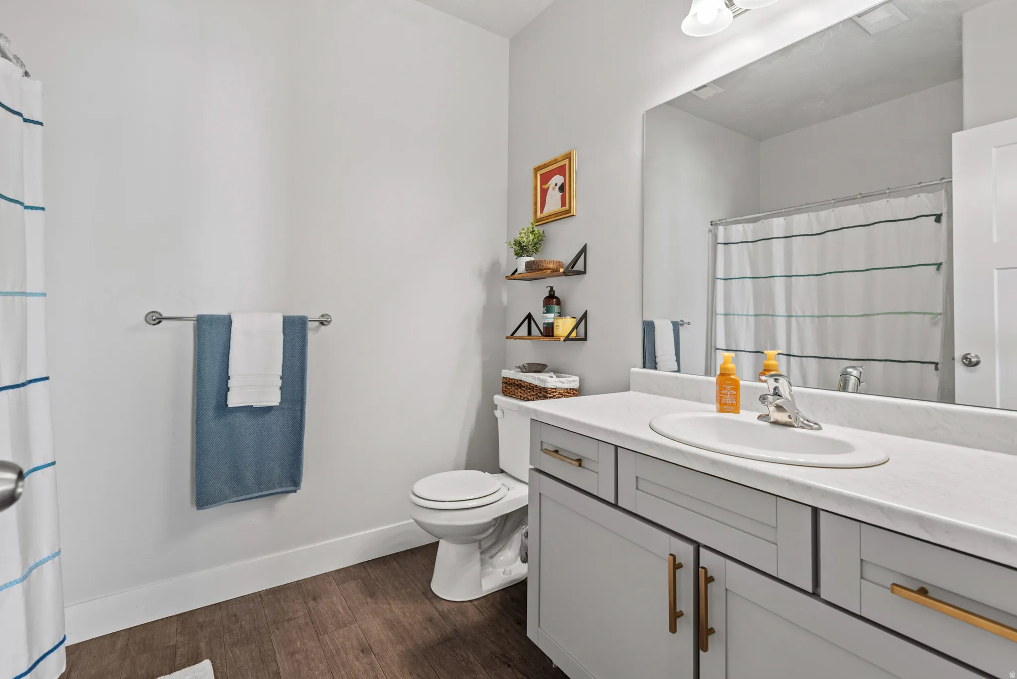 Bathroom featuring a single vanity with light grey cabinetry and contemporary brass hardware, an integrated sink, and a large wall-mounted mirror