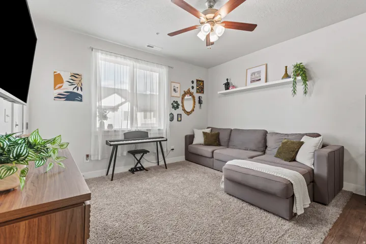 Carpeted room featuring a ceiling fan with light fixture, natural light through a double window, and a wall-mounted floating shelf