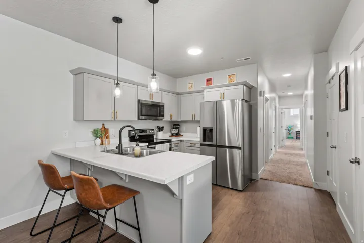 Kitchen featuring light grey cabinetry with gold-tone hardware, stainless steel appliances, a white countertop island with a built-in sink and matte black faucet, and wood-finish flooring
