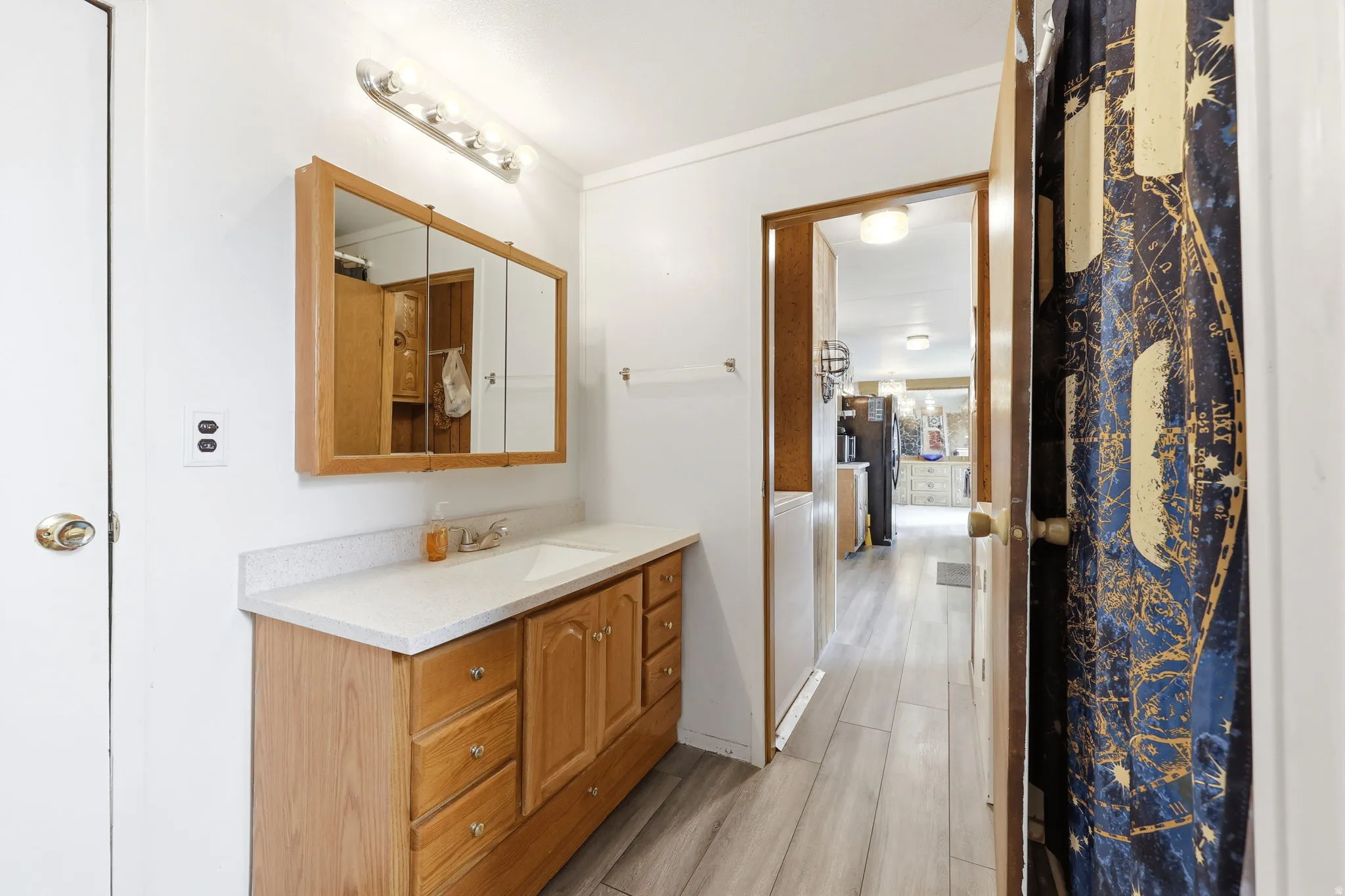 Bathroom vanity with light wood-finish cabinetry, a white countertop, and an integrated sink