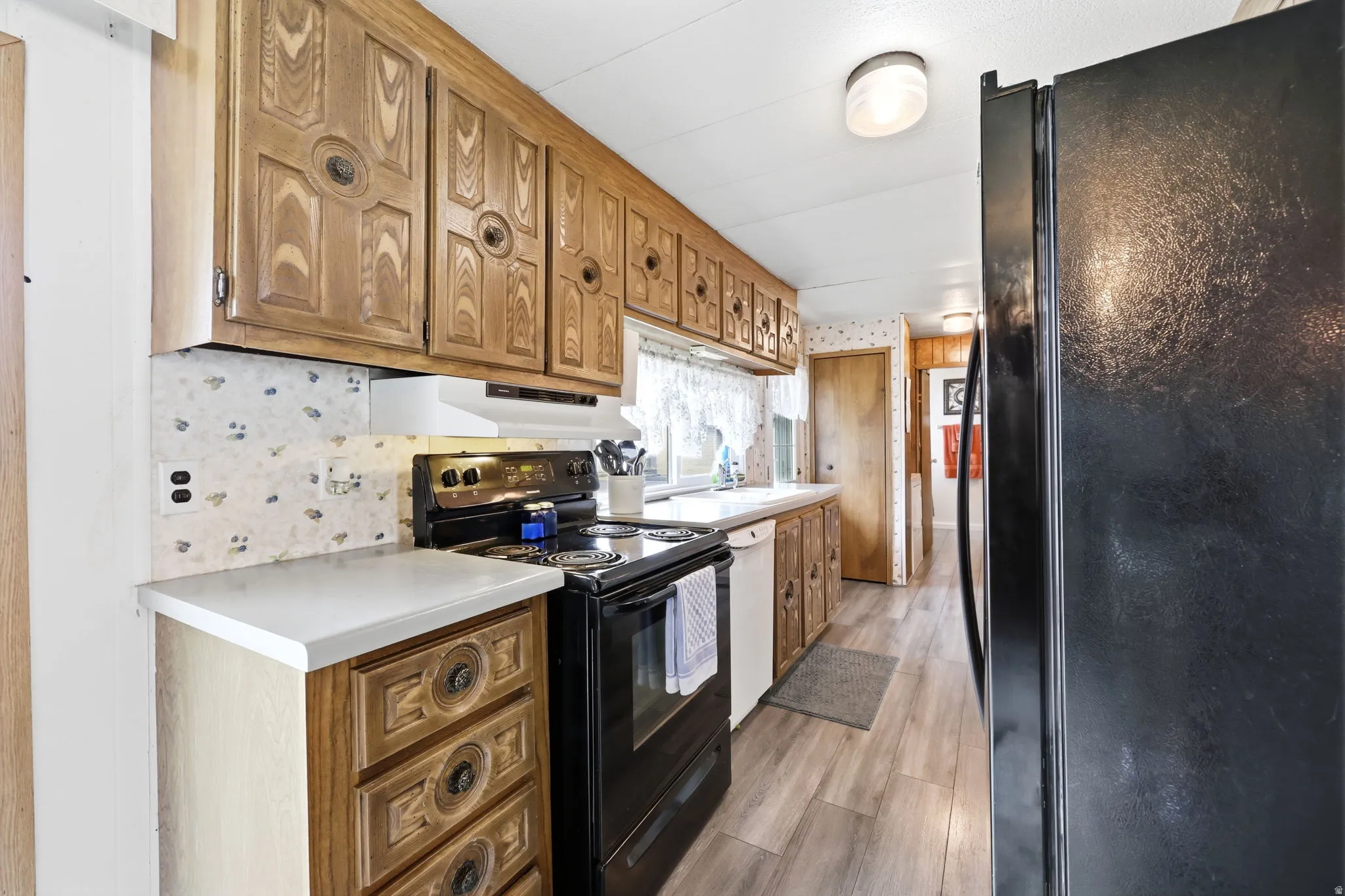 Kitchen featuring wood cabinetry, white countertops, a black electric range, a black refrigerator, and wood-finish flooring