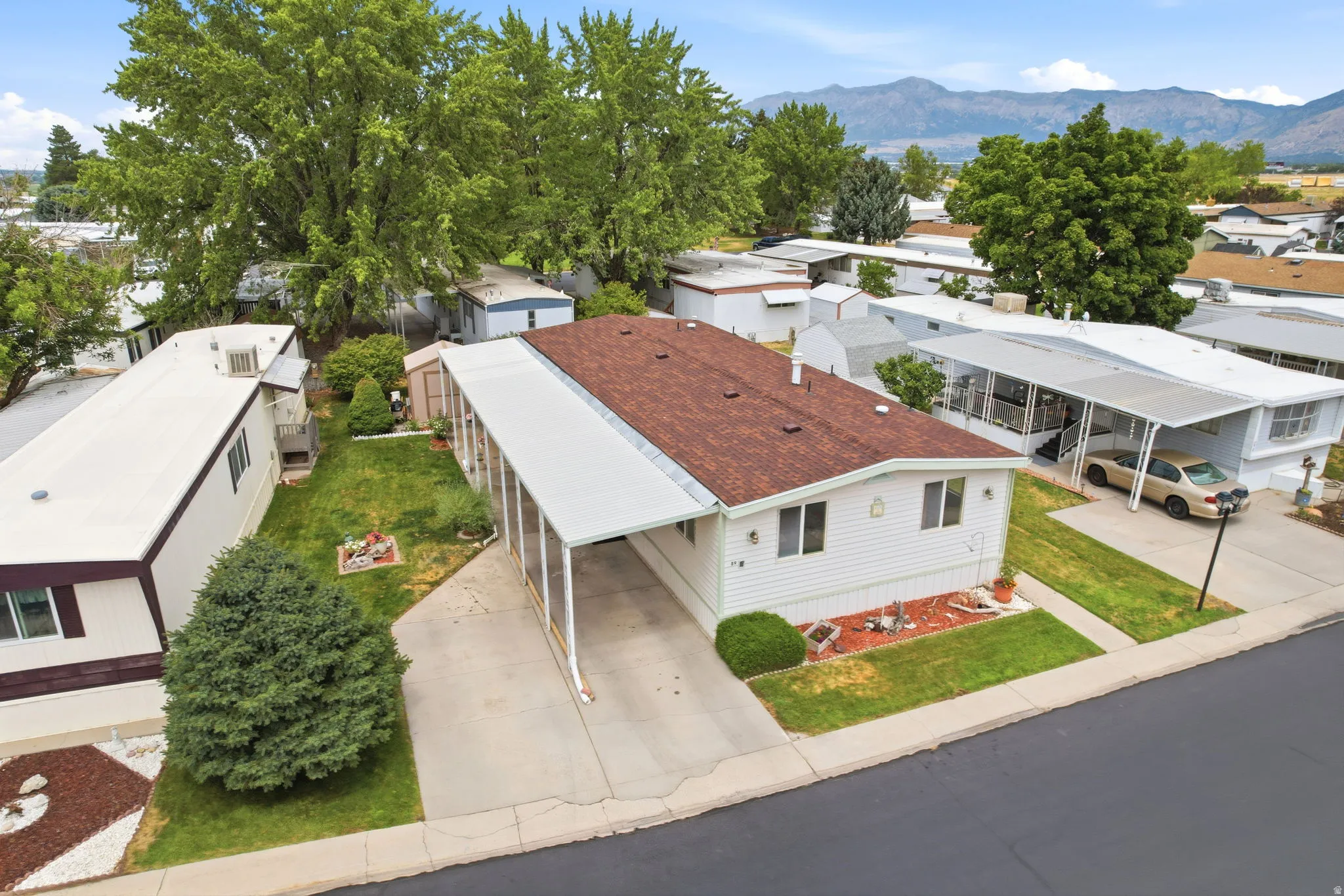 White siding residence featuring a covered carport, pitched shingle roof, green lawn, and mature landscaping