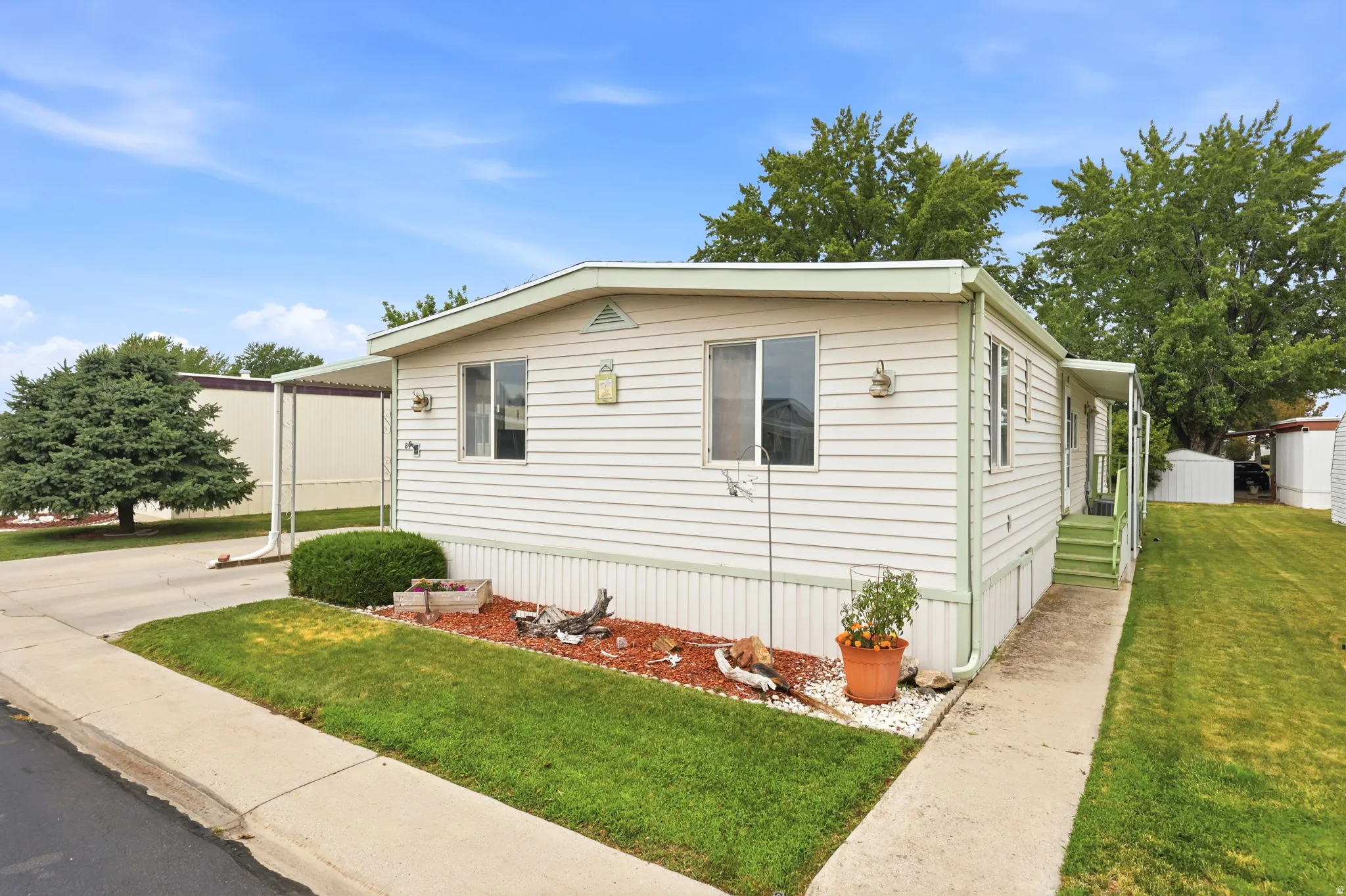 Single-story residence featuring light-colored siding, a covered entry, established landscaping, and a paved walkway