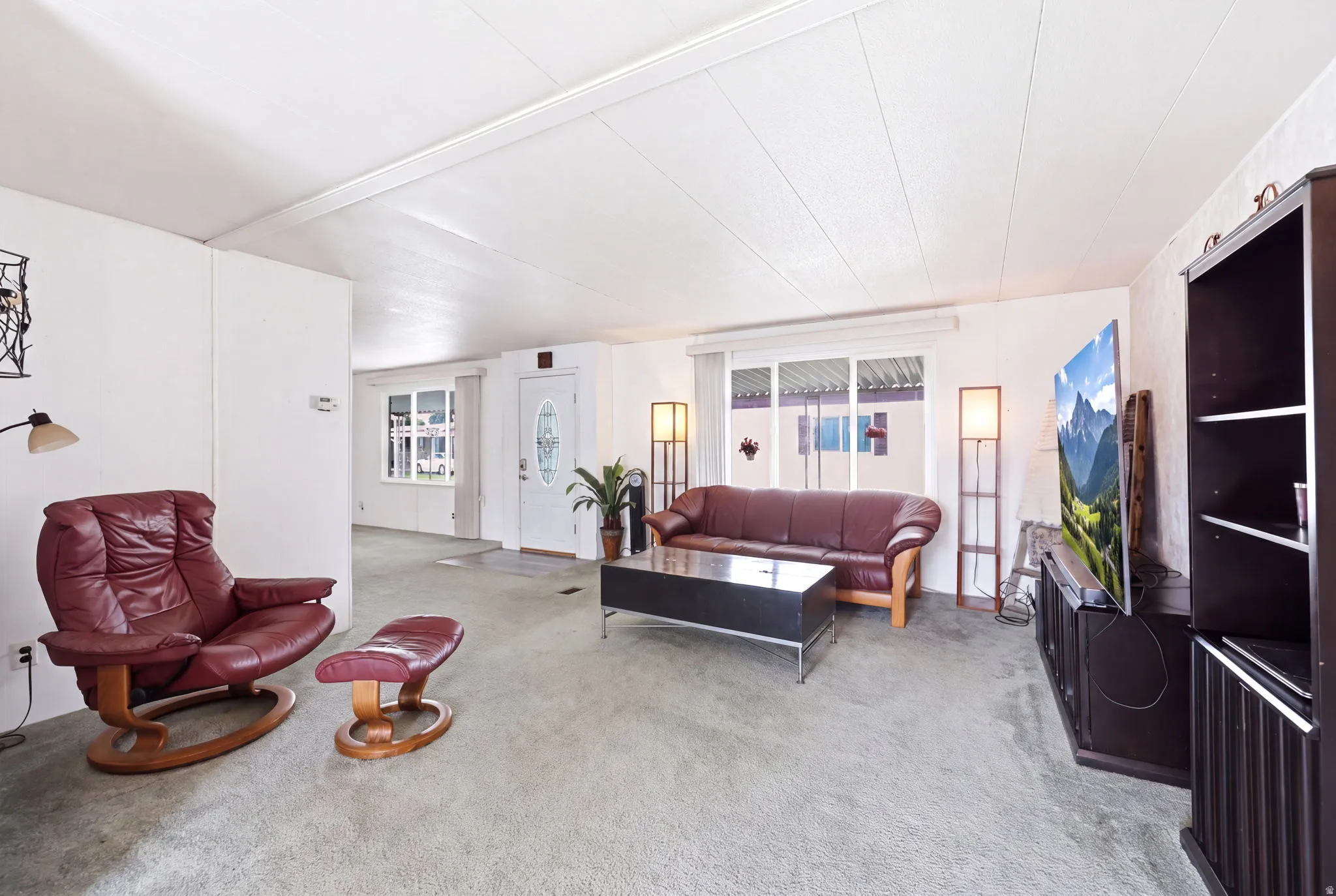 Spacious living area featuring light-colored wall panels, textured ceiling, and light gray carpeted flooring