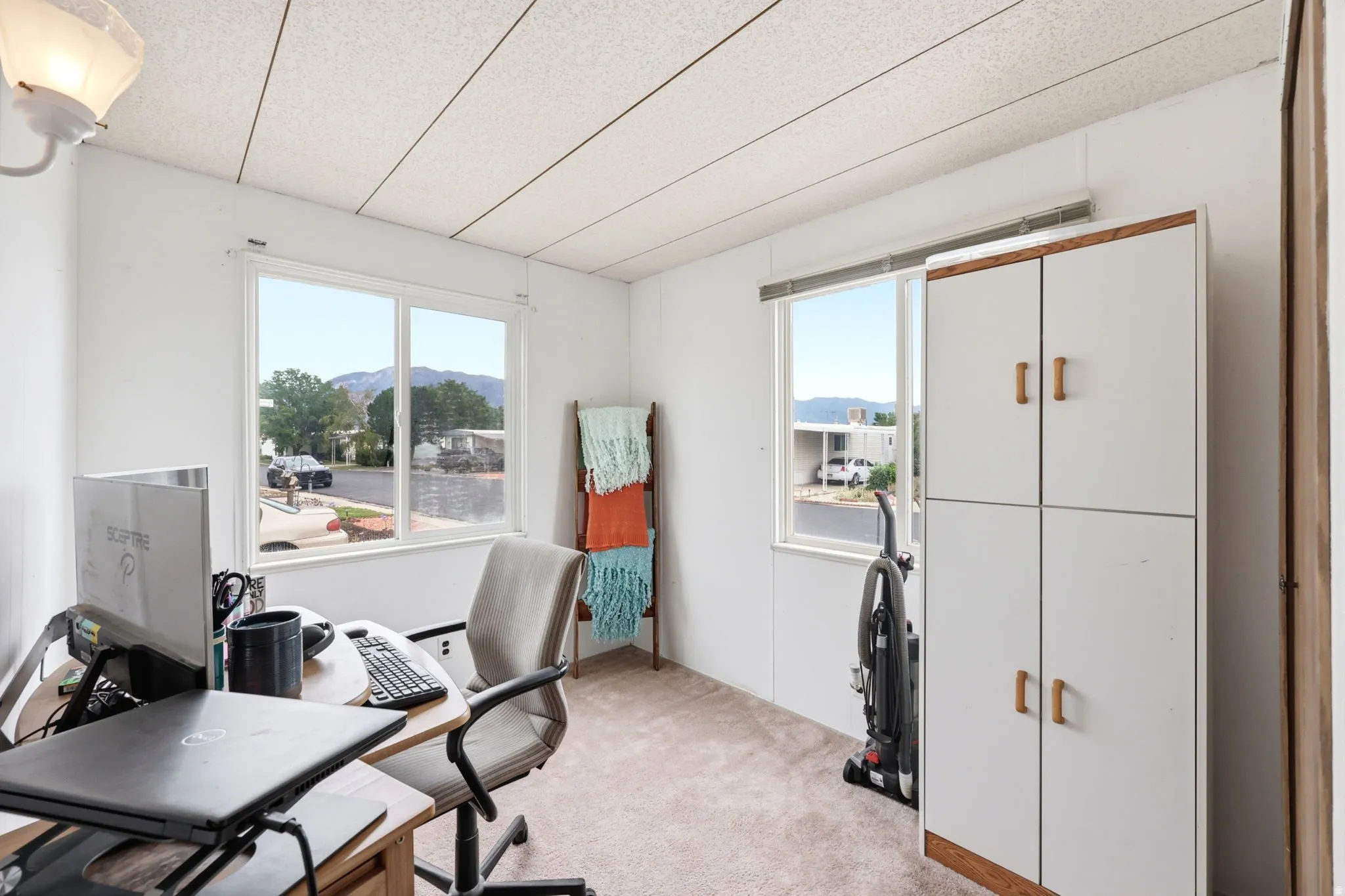 Light-filled interior space with two windows, showcasing a built-in storage cabinet with wood-finish accents and a textured ceiling