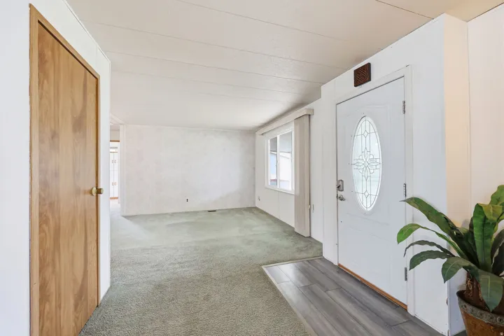 Front entry featuring a white door with decorative oval glass insert, wood-finish flooring, and a spacious living area with green carpet