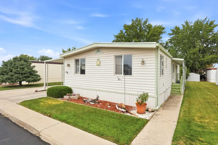 Single-story residence featuring light-colored siding, a covered entry, established landscaping, and a paved walkway