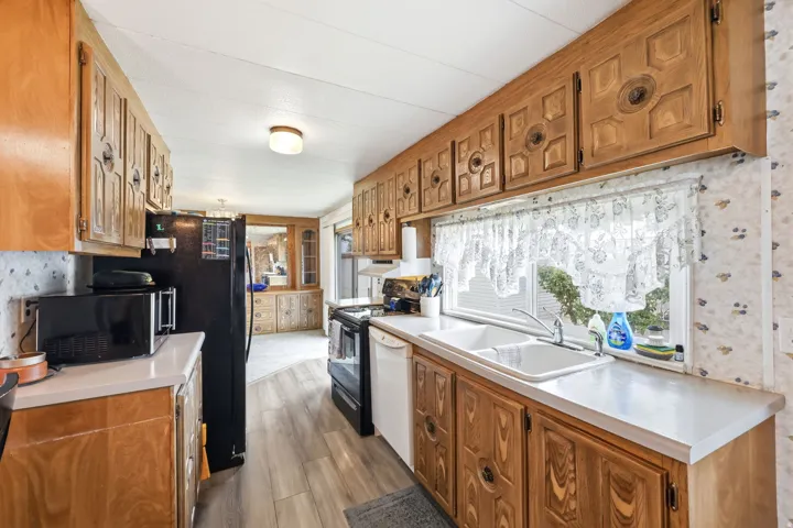 Kitchen featuring abundant wood cabinetry, white countertops, dual-basin sink with window, and wood-finish flooring