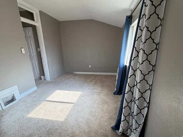 Carpeted room featuring a ceiling-mounted light fixture, angled wall, and window with patterned curtains
