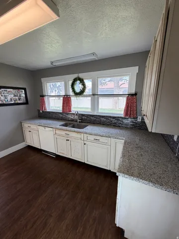 Kitchen featuring wood-finish flooring, white cabinetry with dark hardware, speckled countertops, and a mosaic tile backsplash