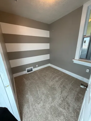 Room featuring textured carpeting, a single window with white trim, and walls with a horizontal stripe pattern