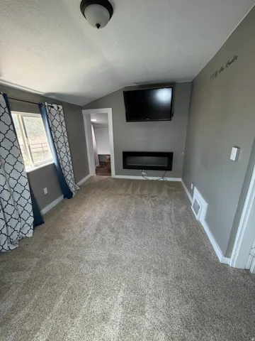 Carpeted room featuring a wall-mounted electric fireplace, a flush-mount ceiling light fixture, and white trim