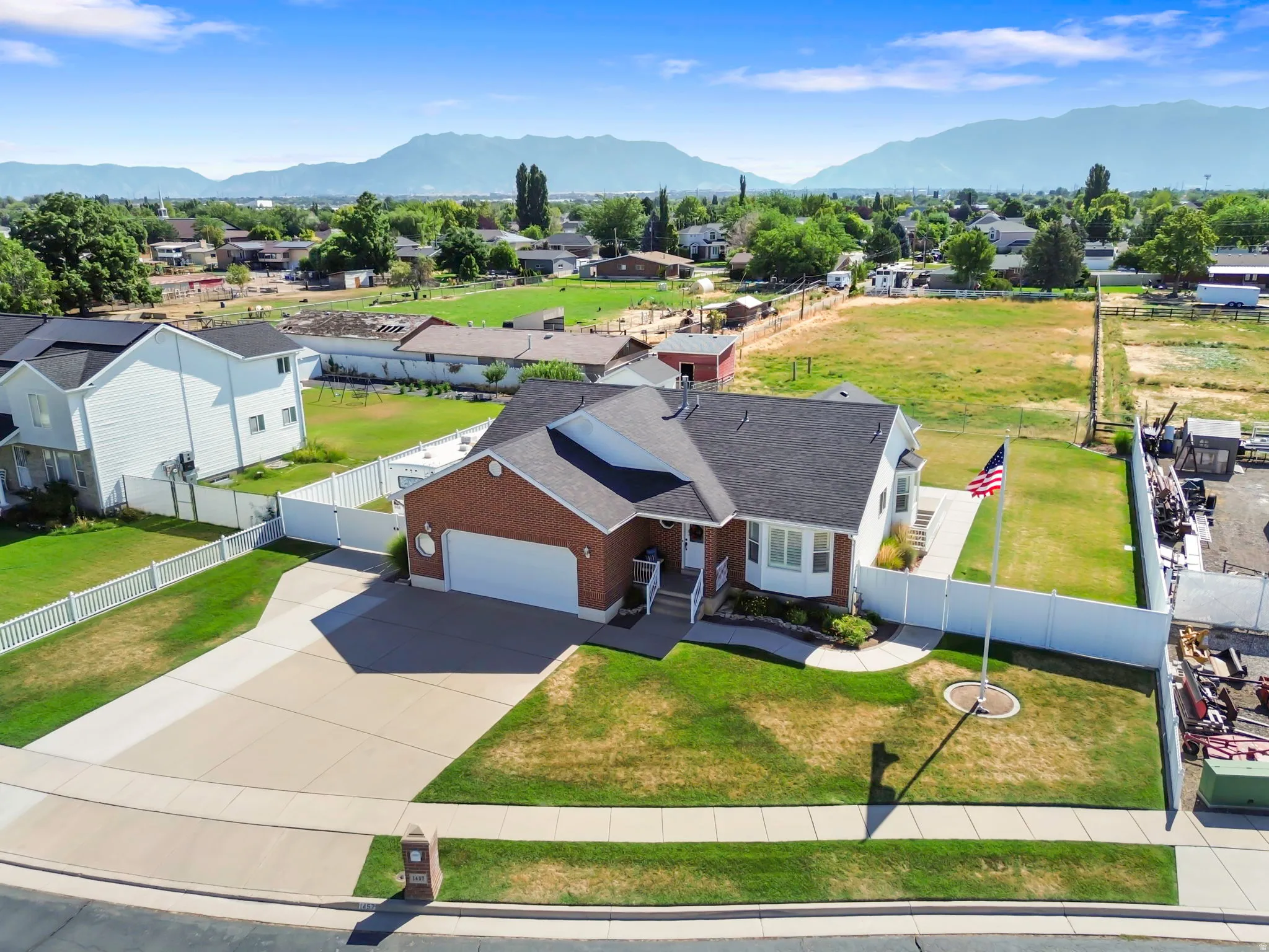 Brick exterior residence with an attached two-car garage, mature landscaping, paved driveway, and a white picket fence