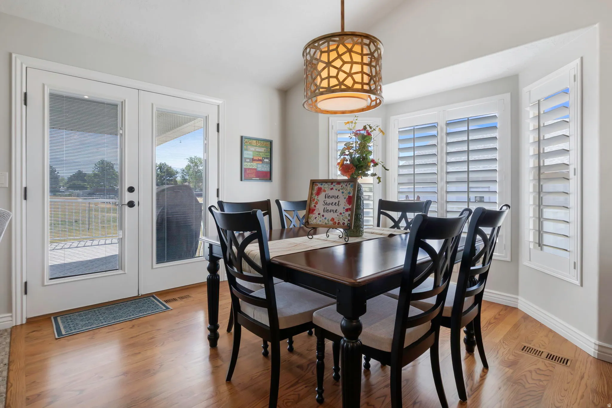 Dining area featuring wood-finish flooring, a decorative pendant light, and a bay window with white plantation shutters