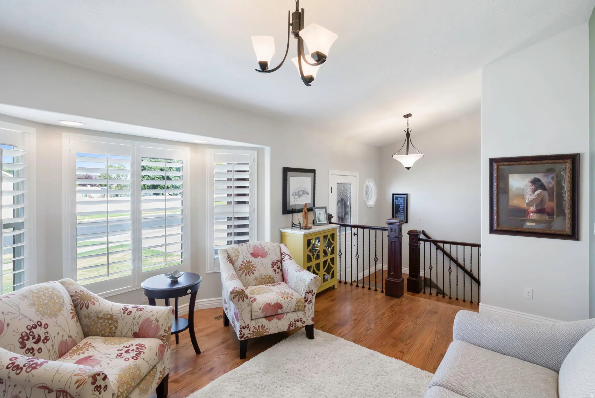 Bay window with plantation shutters, wood-finish flooring, wrought iron staircase railing with wood newel posts, and recessed ceiling lighting