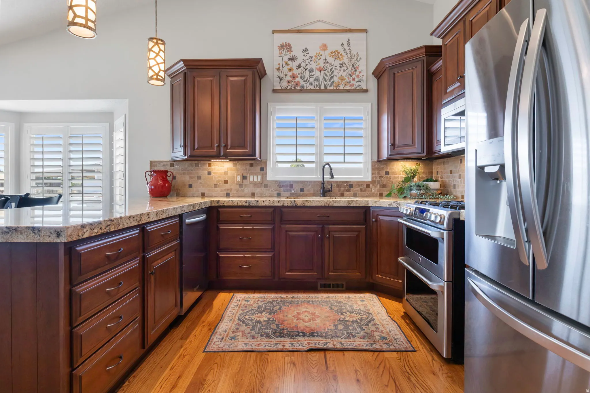 Kitchen featuring rich wood cabinetry, granite countertops, stainless steel appliances, a tiled backsplash, and wood-finish flooring
