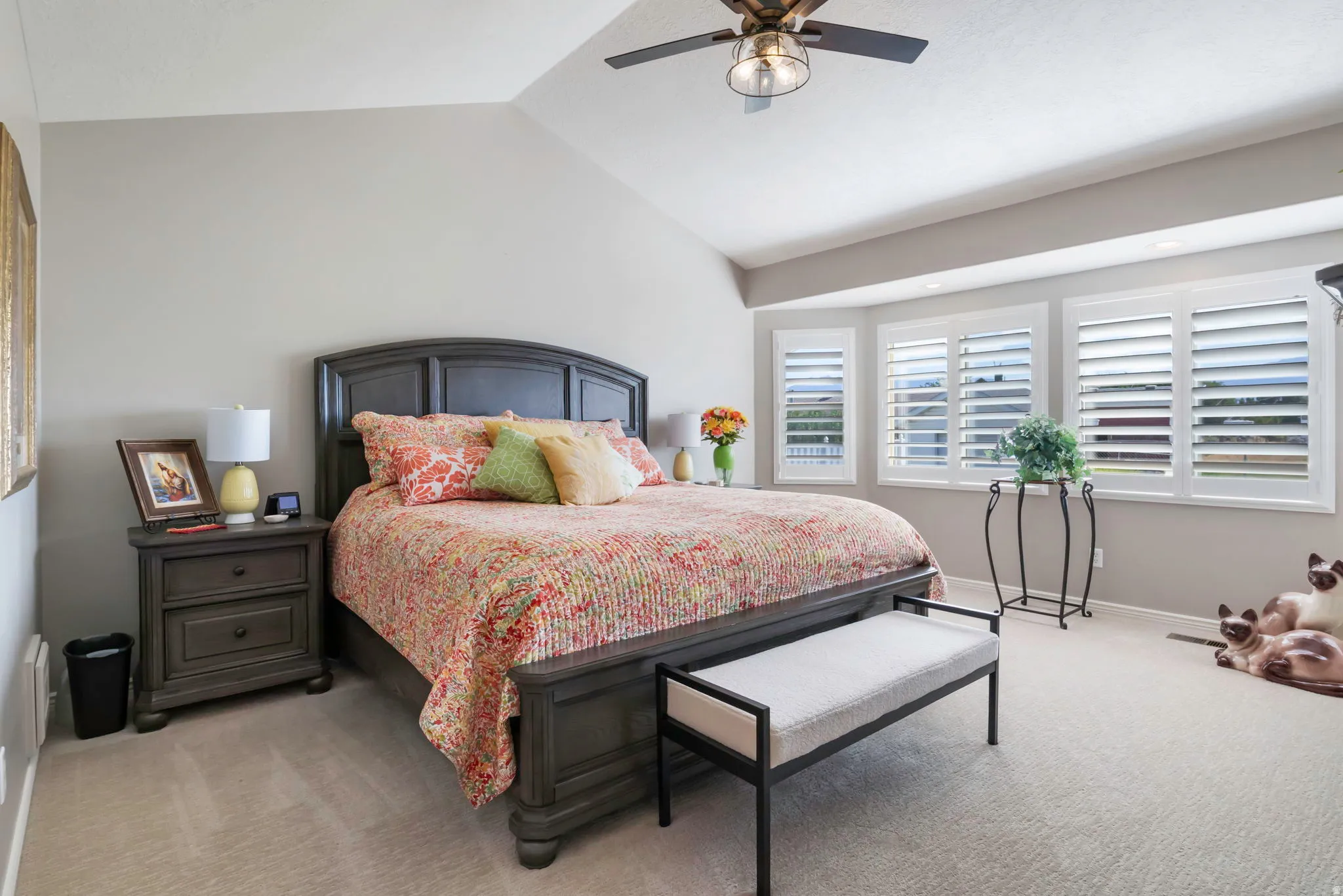 Spacious bedroom featuring vaulted ceilings, a ceiling fan with integrated lighting, a bay window with plantation shutters, and plush carpet flooring