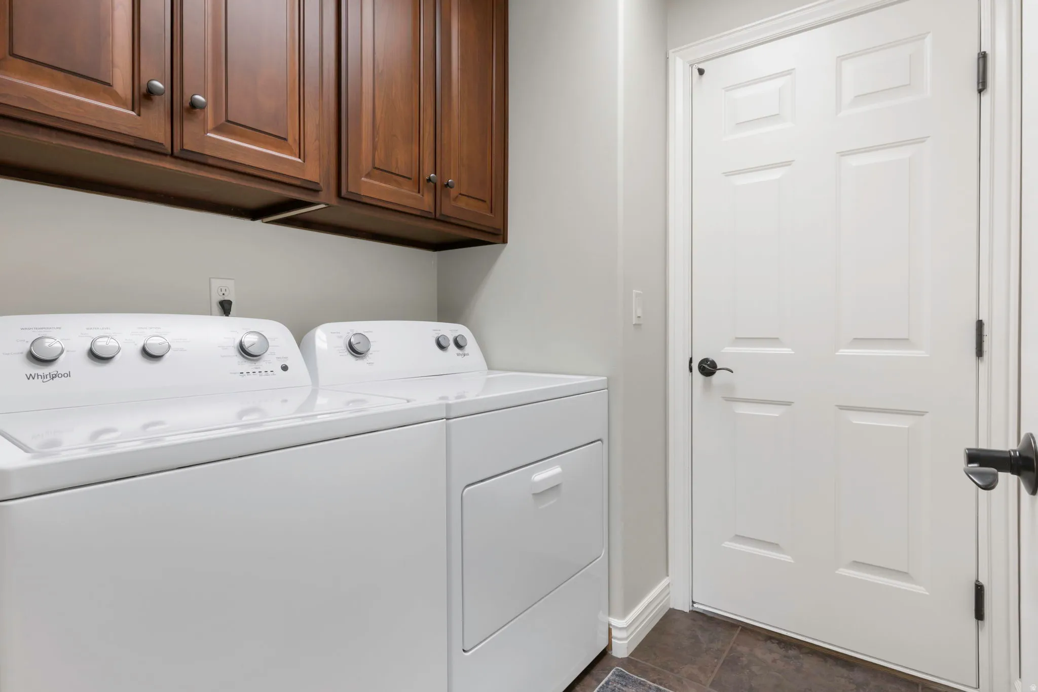 Laundry area featuring overhead wood cabinetry, a paneled door, and dark tile flooring
