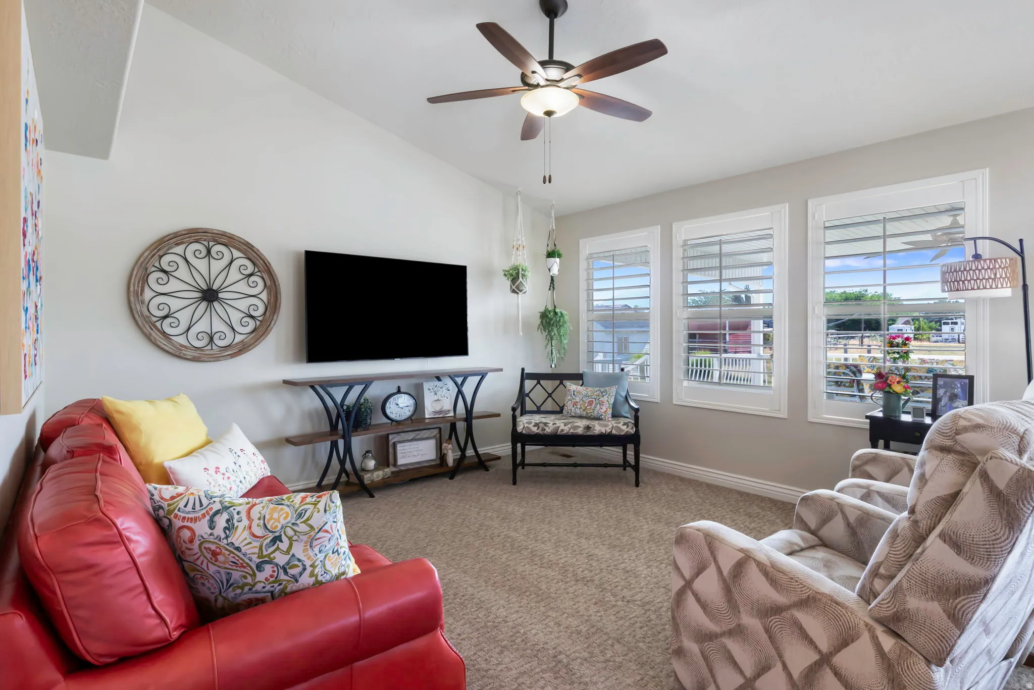 Vaulted ceiling with a ceiling fan, three windows with white plantation shutters, and light-toned wall paint