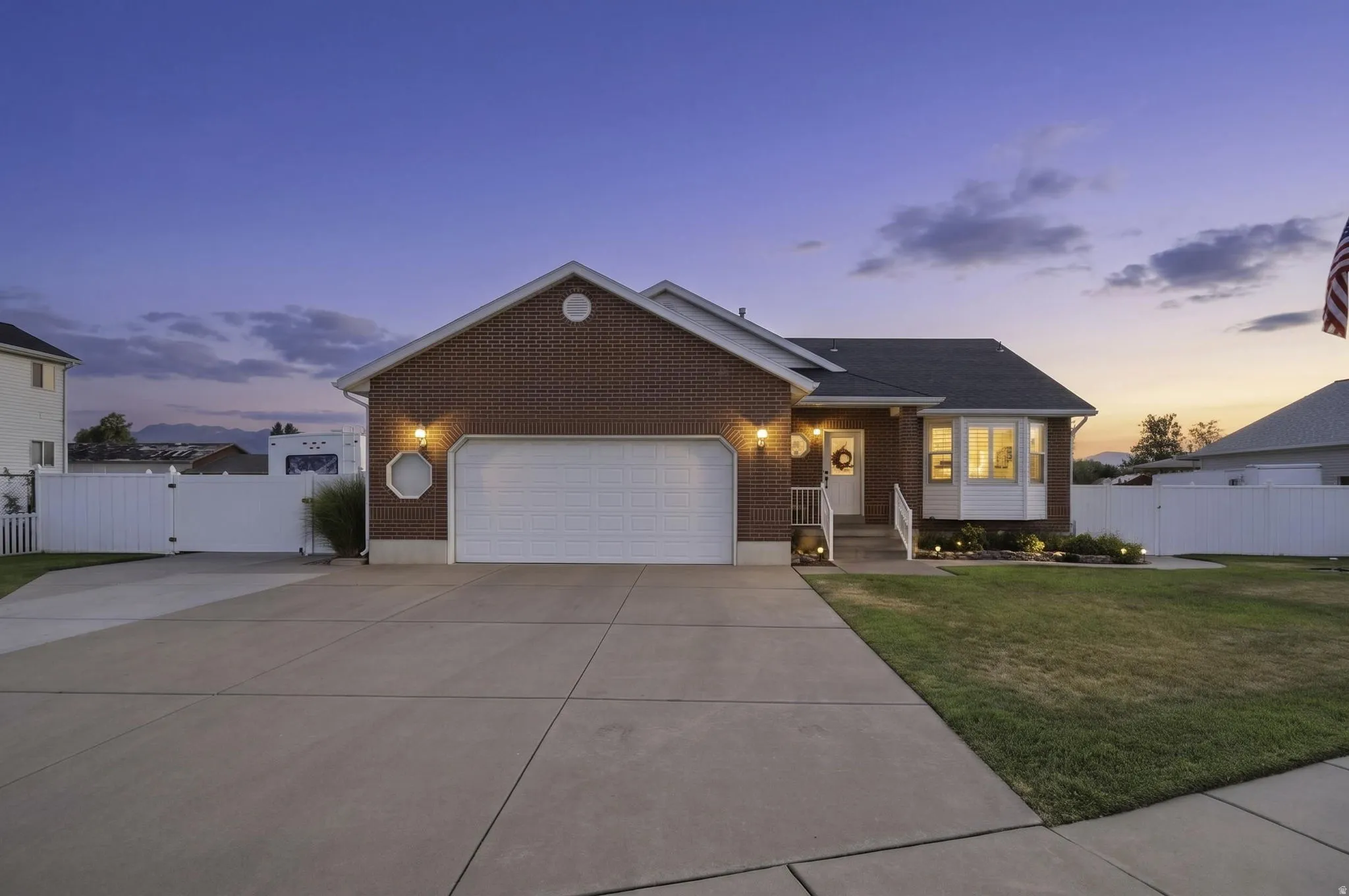 Brick exterior featuring a two-car garage, concrete driveway, bay window, and a white picket fence