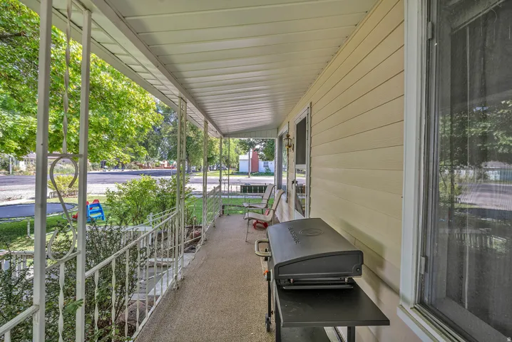 Covered porch with white metal railings, beige horizontal siding, and textured flooring
