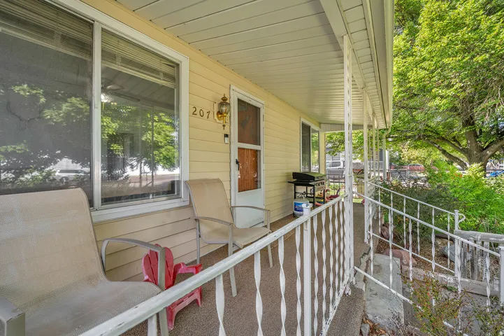 Inviting covered front porch with white metal railings, light yellow siding, and a decorative outdoor light fixture