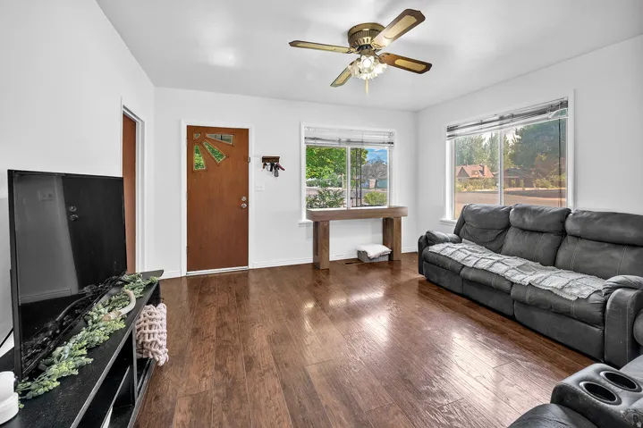 Living area featuring wood-finish flooring, a ceiling fan with integrated lighting, and multiple windows