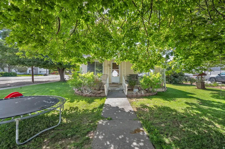 Charming single-story residence with a covered front porch, concrete pathway, expansive lawn, and mature shade trees