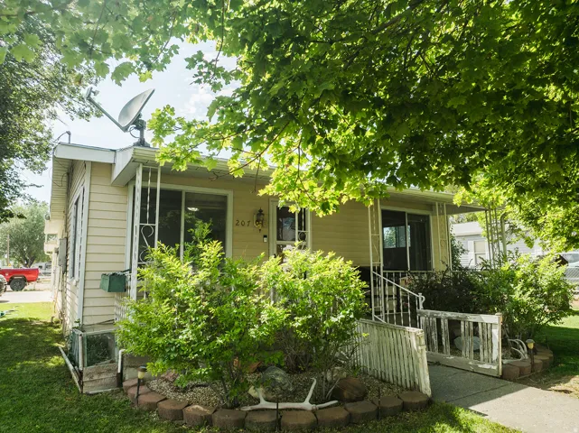Exterior residence with light-colored siding, a covered porch entrance, and mature landscaping
