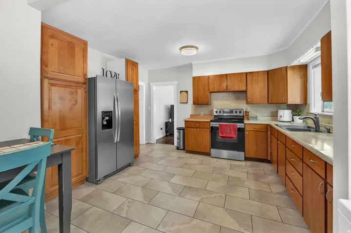 Kitchen featuring wood cabinetry, stainless steel appliances, light-toned countertops, and tile flooring