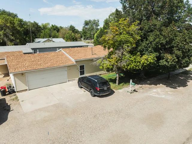 Single-story residence featuring light siding, an attached garage, a driveway, and mature trees