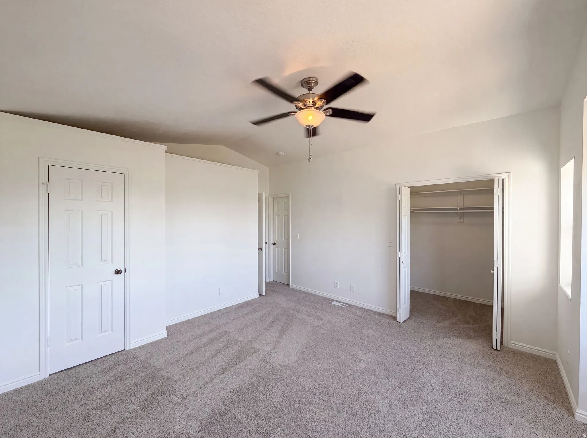 Spacious room featuring neutral carpeting, white walls, a ceiling fan with integrated lighting, a bi-fold closet with shelving, and multiple windows for natural light