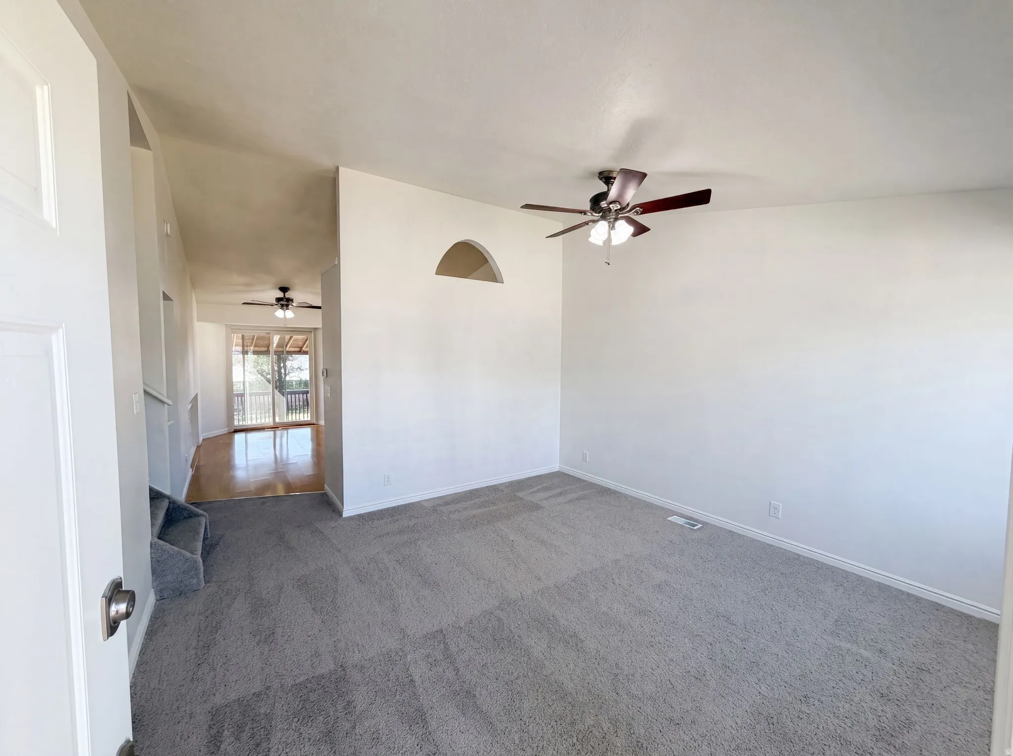 Spacious room featuring neutral carpeting, a ceiling fan with light, and an arched wall opening