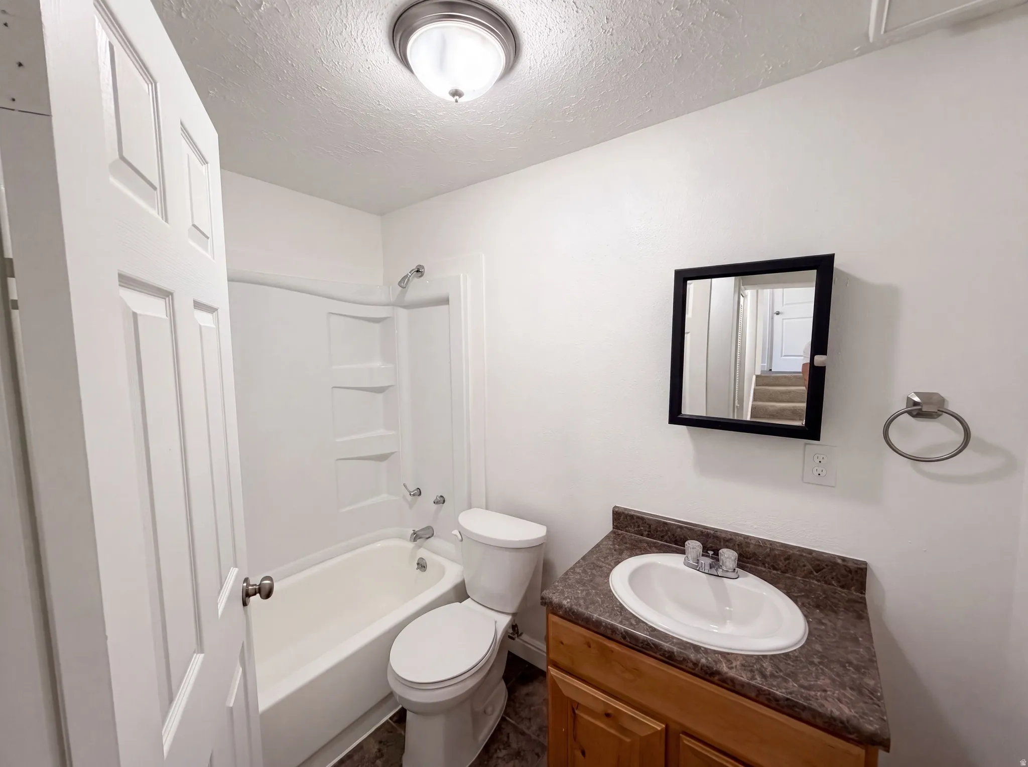 Full bathroom featuring a white tub and shower combination with an integrated storage shelf, a toilet, and a wood-finish vanity with an oval sink and a dark countertop