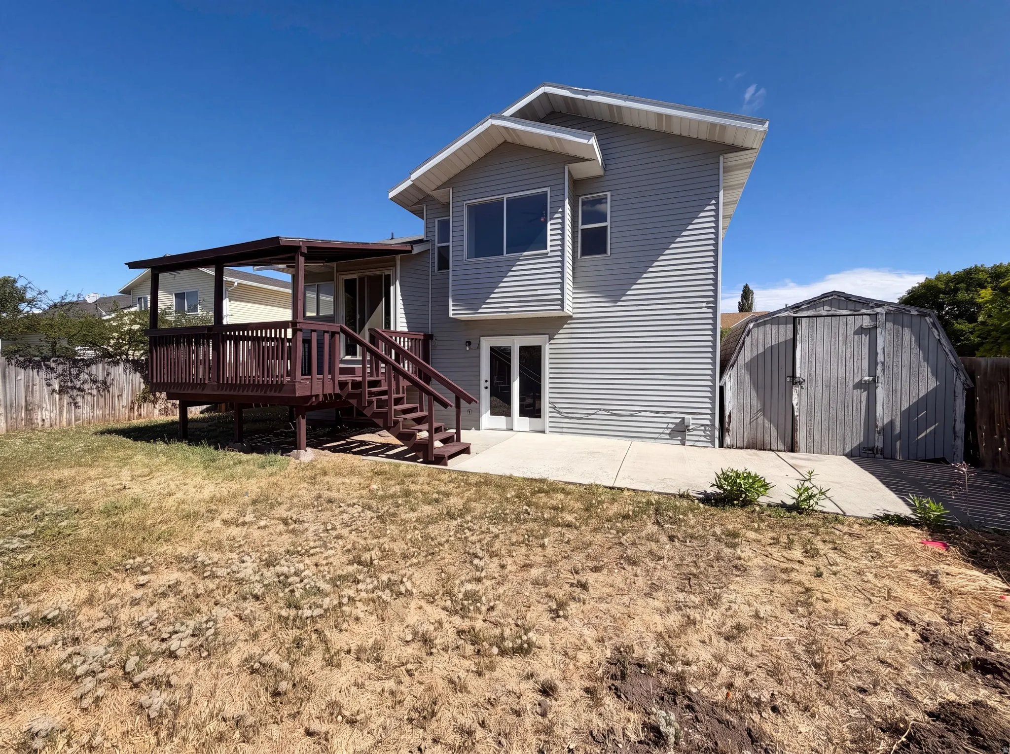 Rear exterior featuring a covered wood deck, concrete patio, and garden shed