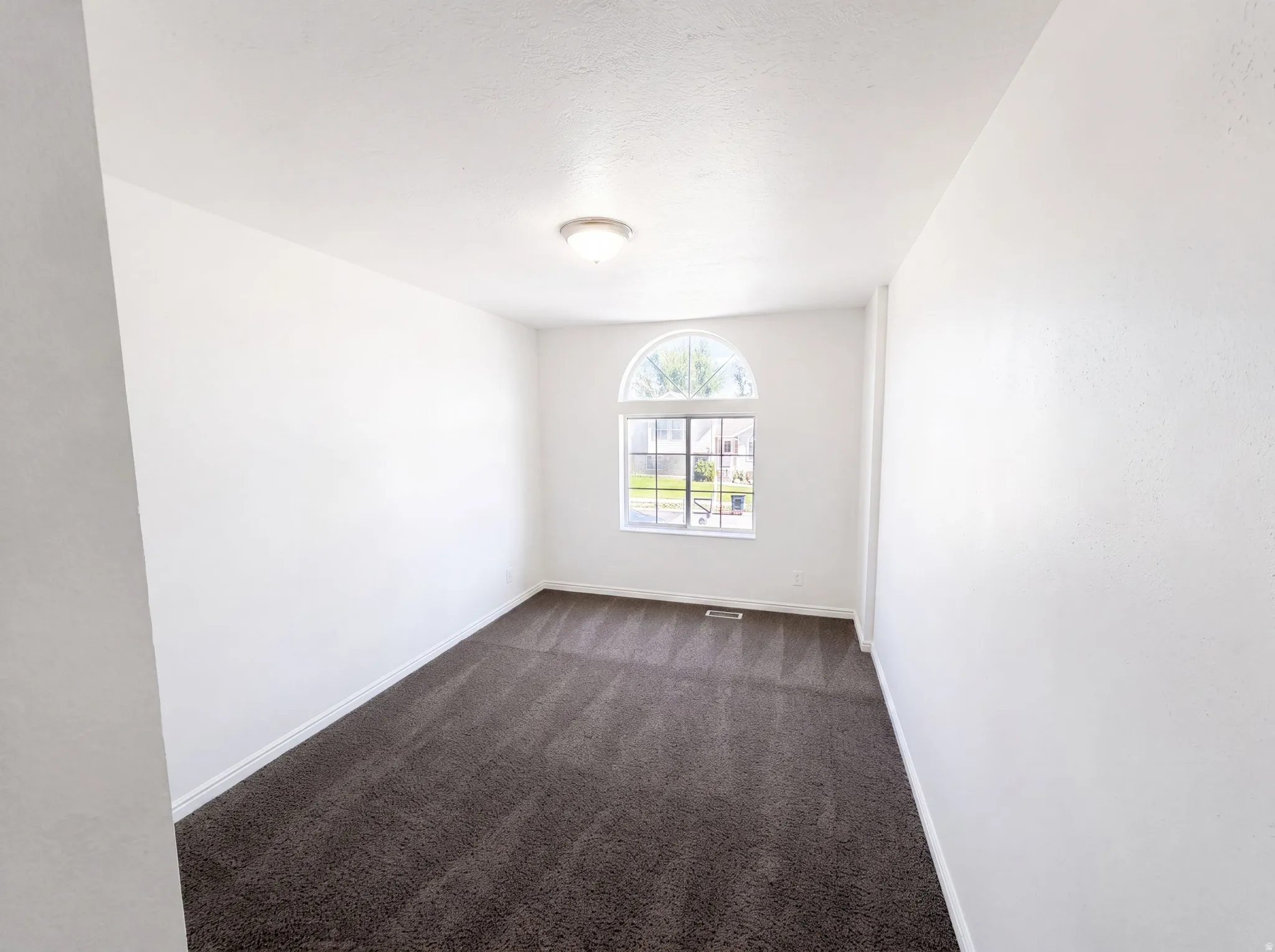 Room featuring an arched window, white walls, dark gray carpet, and a flush mount ceiling light fixture