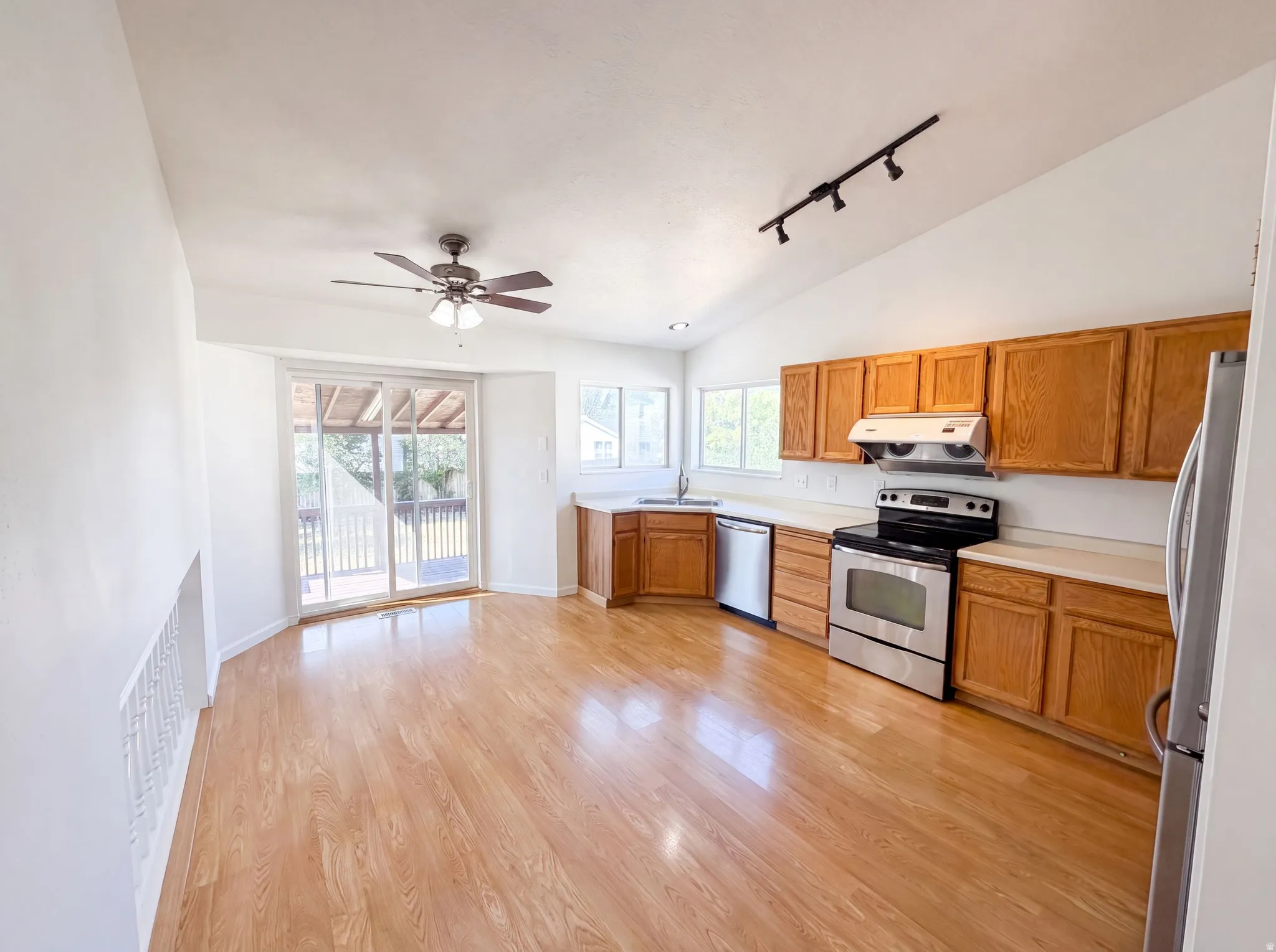 Open-concept space featuring wood-finish flooring, vaulted ceilings, and a kitchen with wood cabinetry and stainless steel appliances