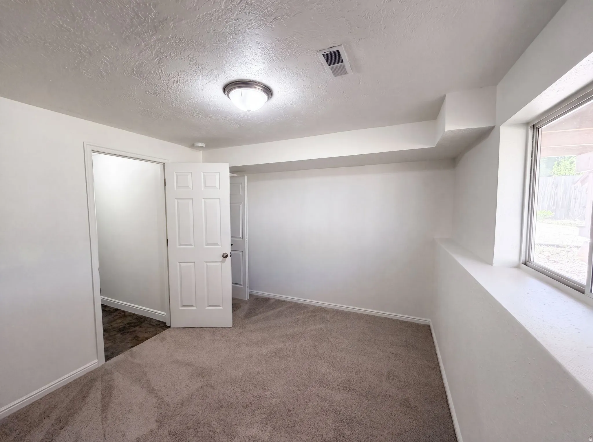 Carpeted room with white walls, a single window, and a flush-mount ceiling light fixture
