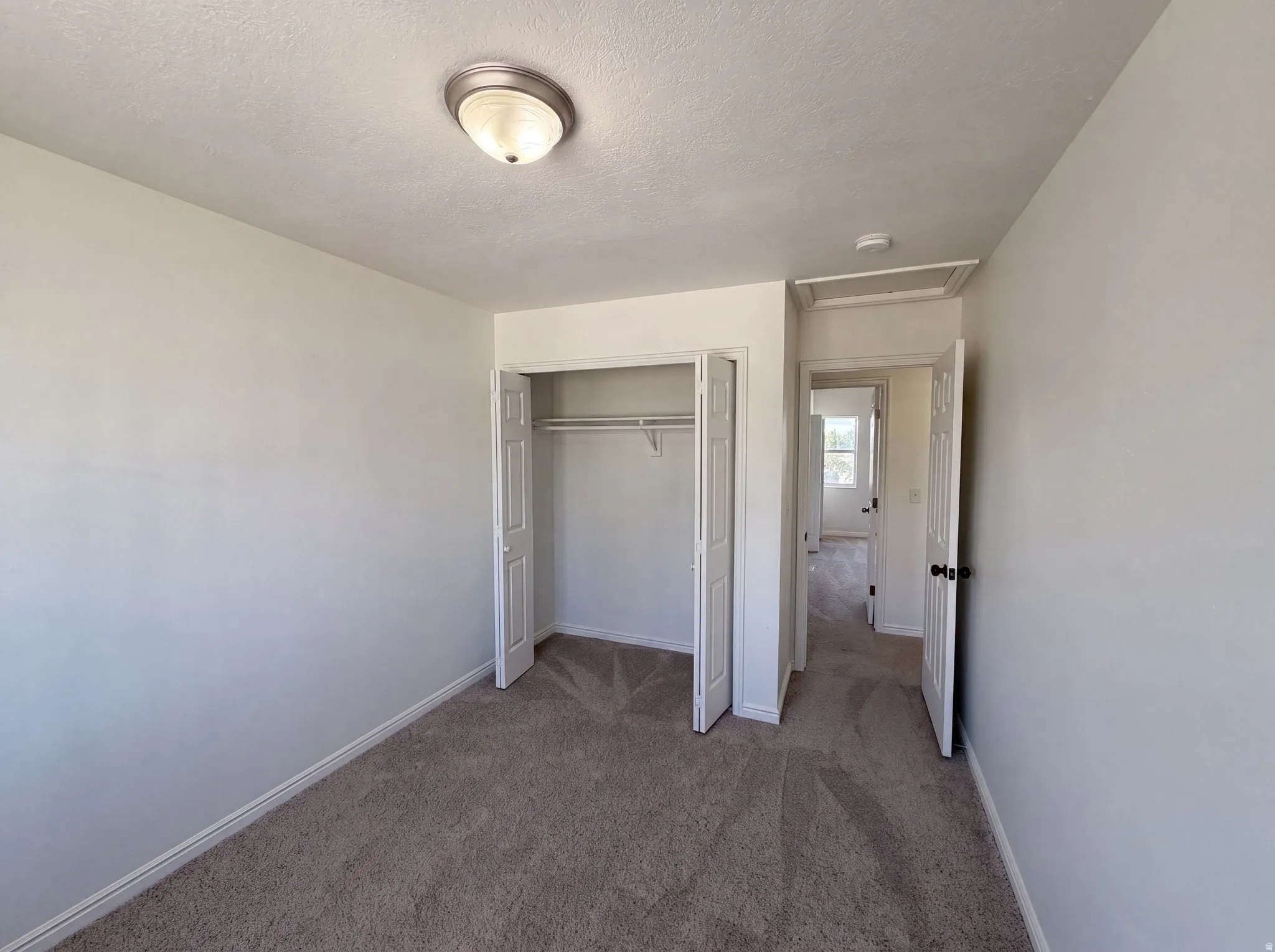 Carpeted room featuring a ceiling-mounted light fixture, bi-fold closet doors, and neutral wall paint