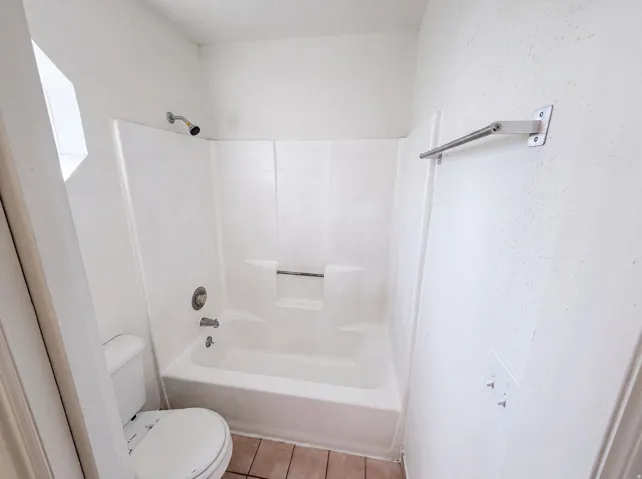 Full bathroom featuring a white tub/shower combination, white toilet, and tile flooring