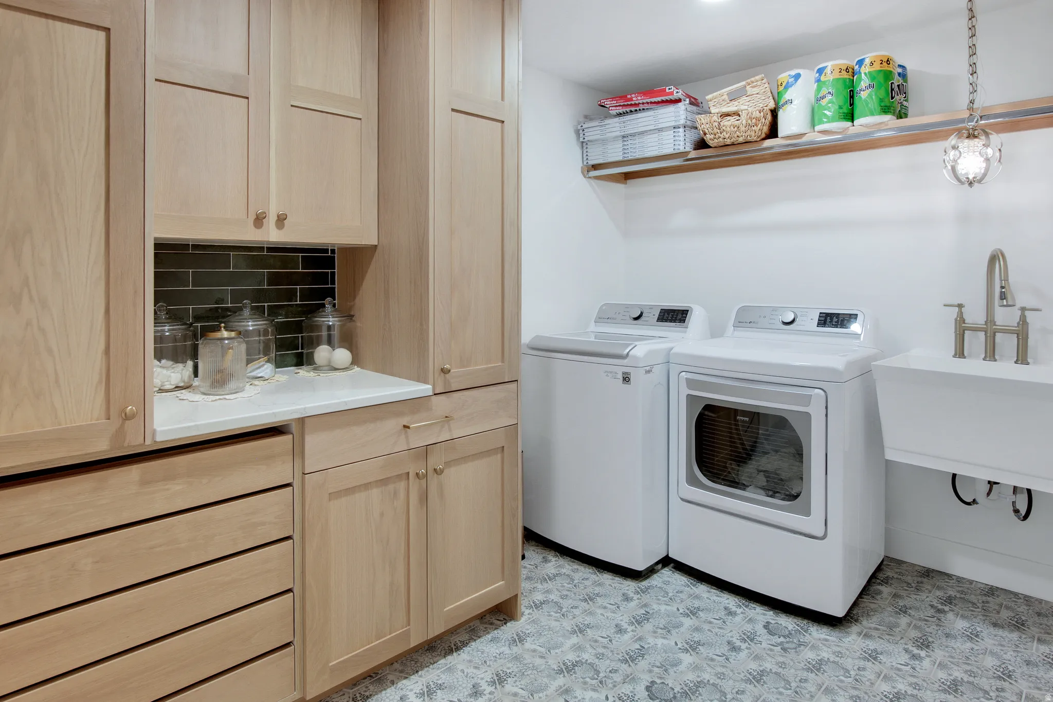 Utility room featuring light wood-finish cabinetry, a white countertop, dark subway tile backsplash, and a patterned floor