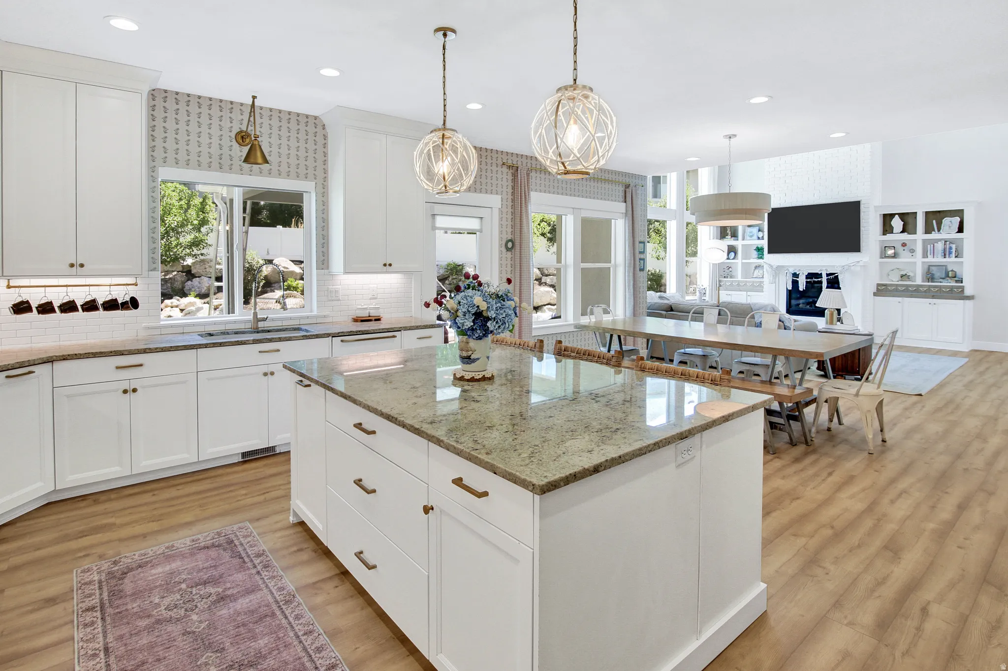 Open-concept kitchen and living area featuring a large center island with stone-finish countertop, white cabinetry with bronze hardware, wood-finish flooring, and two modern spherical pendant lights