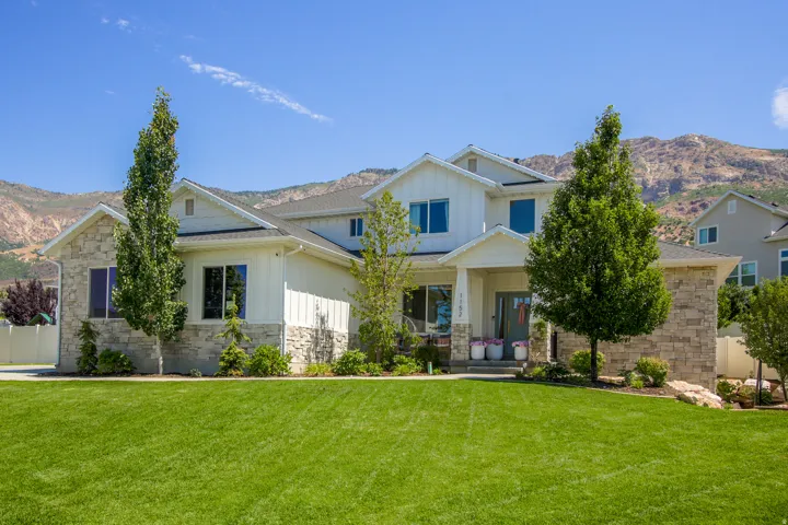 Two-story residence featuring a stone and board and batten facade, a covered front porch, and a professionally landscaped front yard with a lush green lawn