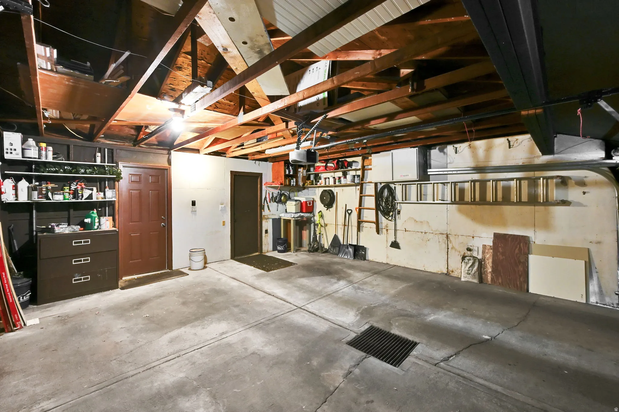 Spacious garage featuring a concrete floor, exposed wood beam ceiling, and two interior access doors