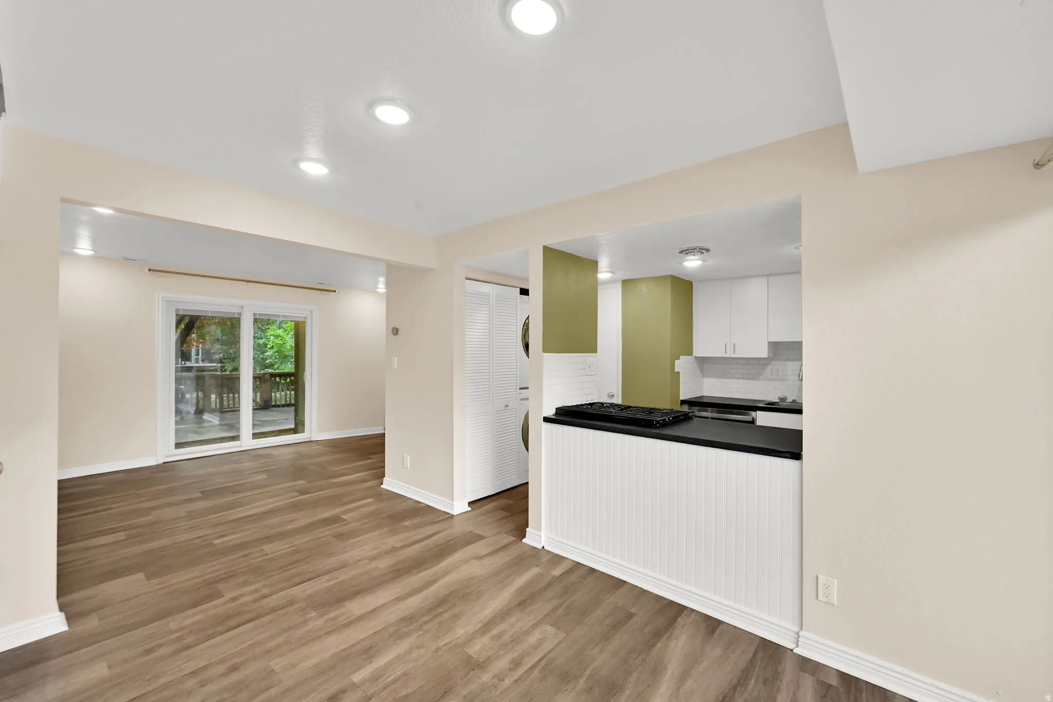 Open-concept living area featuring wood-finish flooring, recessed lighting, and a sliding glass door leading to an outdoor deck