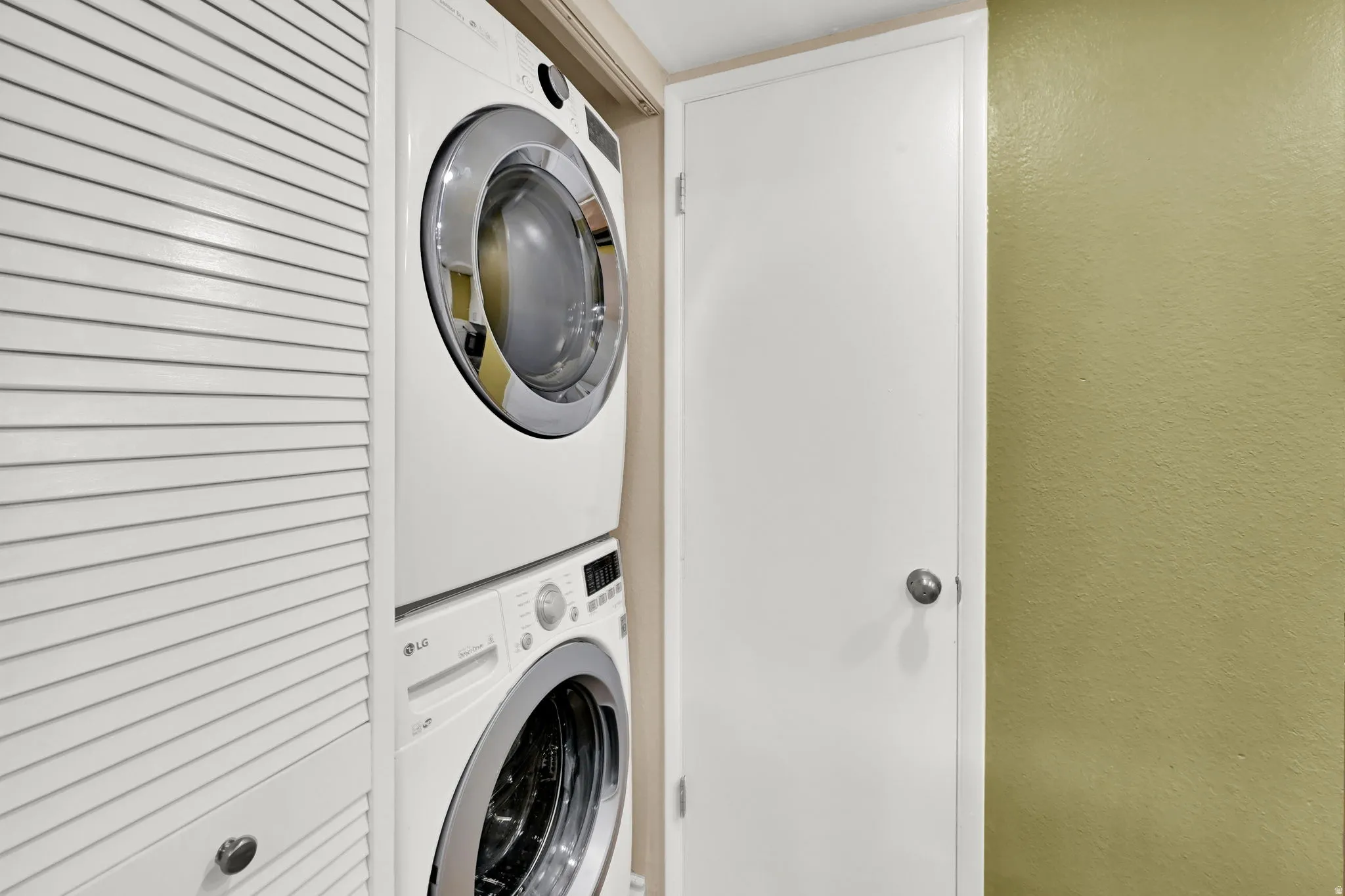 Stackable laundry system with white appliances and chrome accents, complemented by louvered bi-fold doors and a solid white door