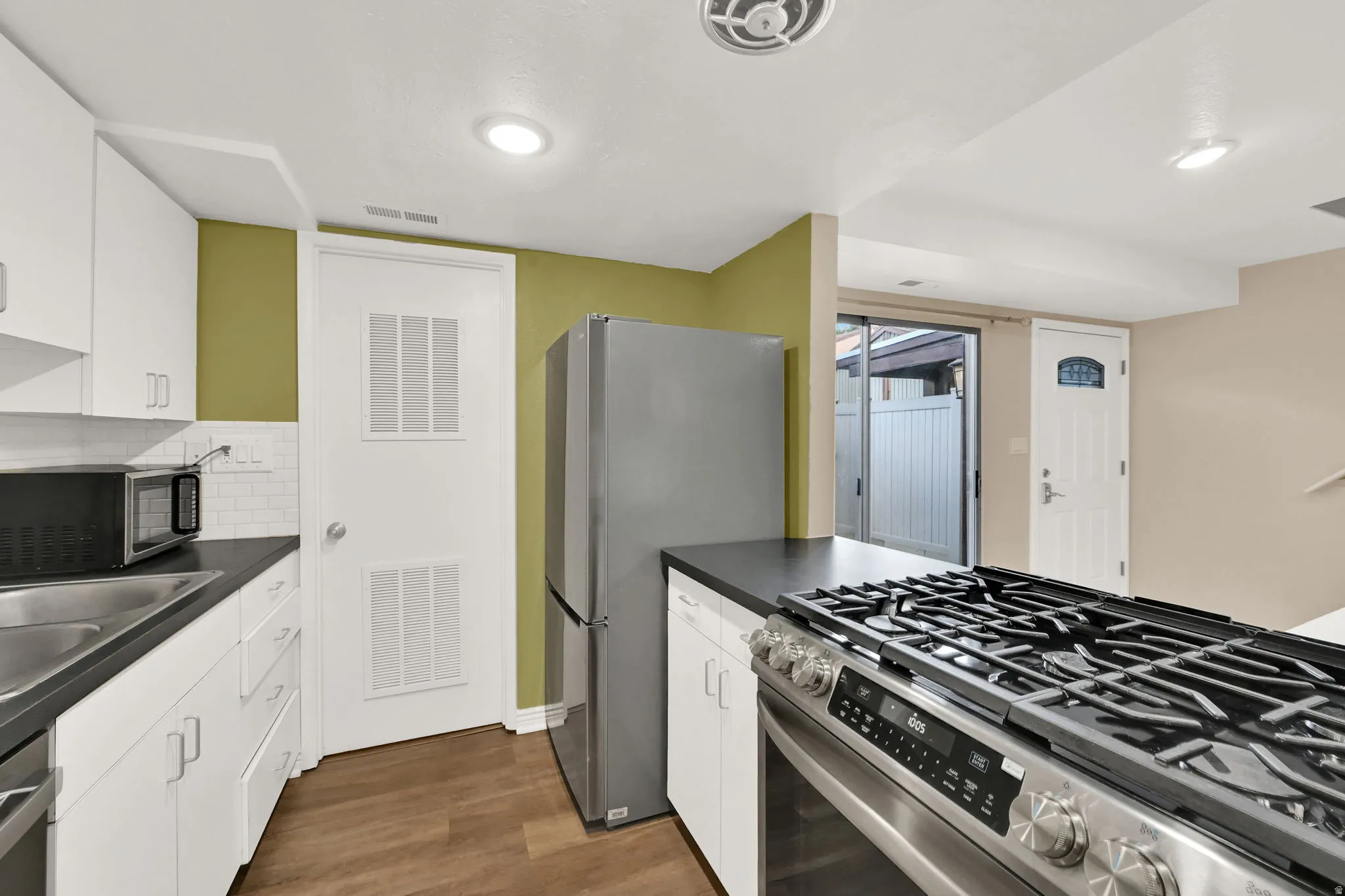 Kitchen featuring a stainless steel range, dark countertops, white cabinetry, wood-finish flooring, and a sliding glass door
