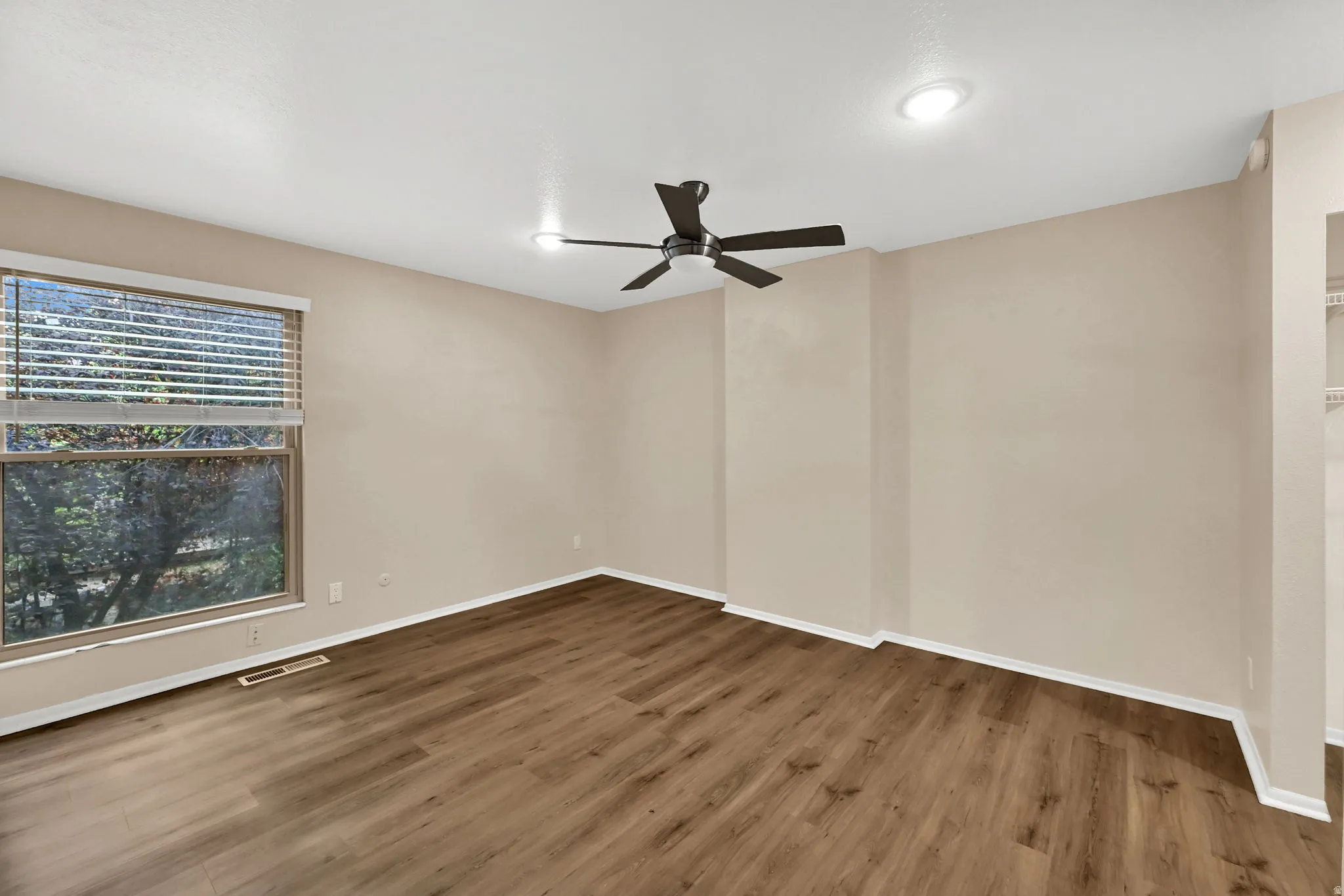 Spacious room featuring wood-finish flooring, a ceiling fan with integrated lighting, recessed lighting, and a large window with blinds