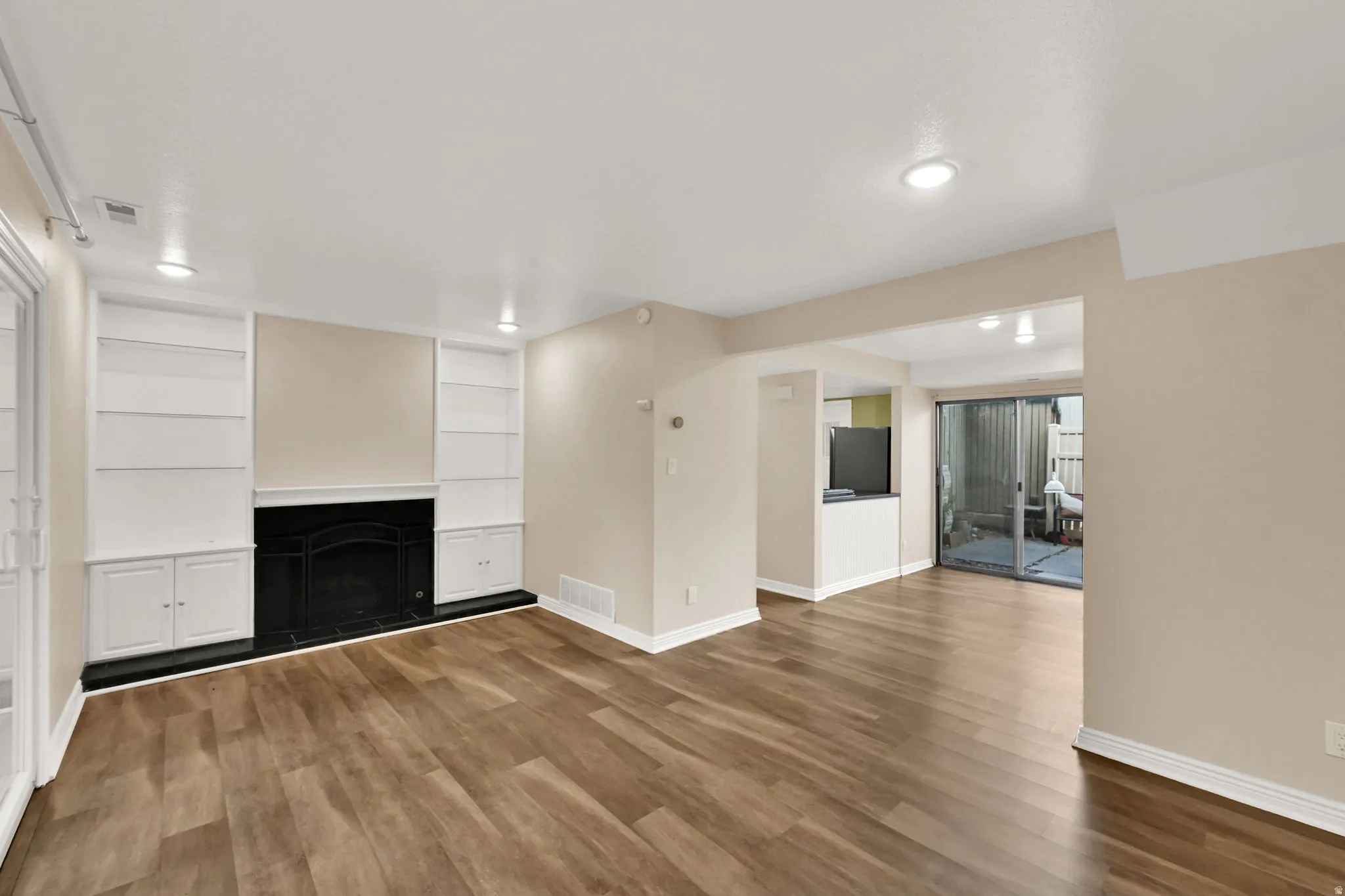 Spacious room featuring wood-finish flooring, a black fireplace with a mantel, built-in shelving, recessed lighting, and direct access to an outdoor patio through sliding glass doors